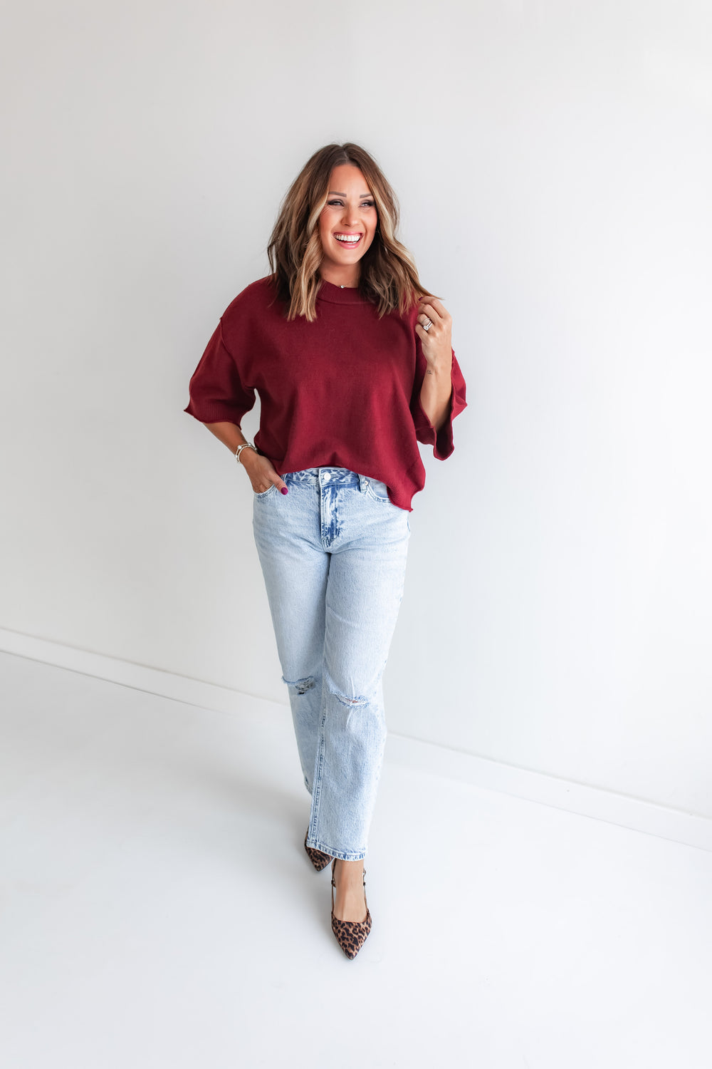 Model wearing slim straight leg light wash denim paired with a rich wine short sleeve sweater top.