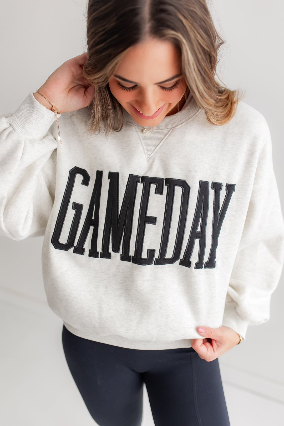 A close-up shot of a heather grey crewneck sweatshirt with "GAMEDAY" embroidered in black on the front.