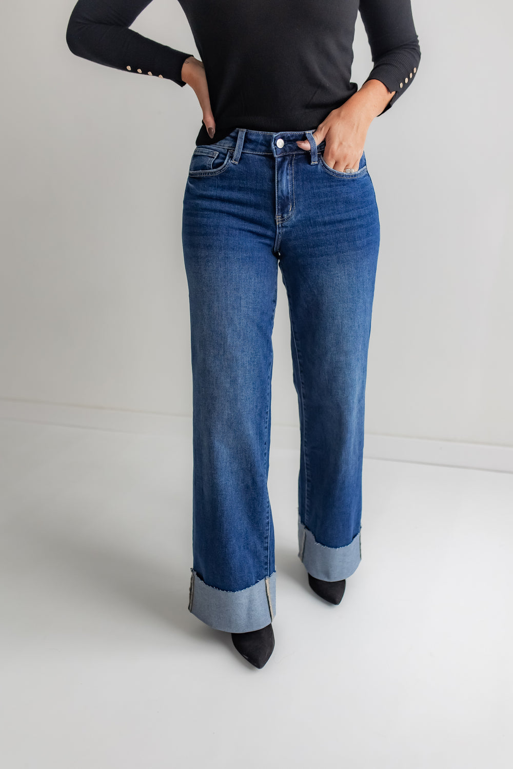  A woman poses in a pair of high-rise, dark-wash wide-leg jeans with a cuffed hem.