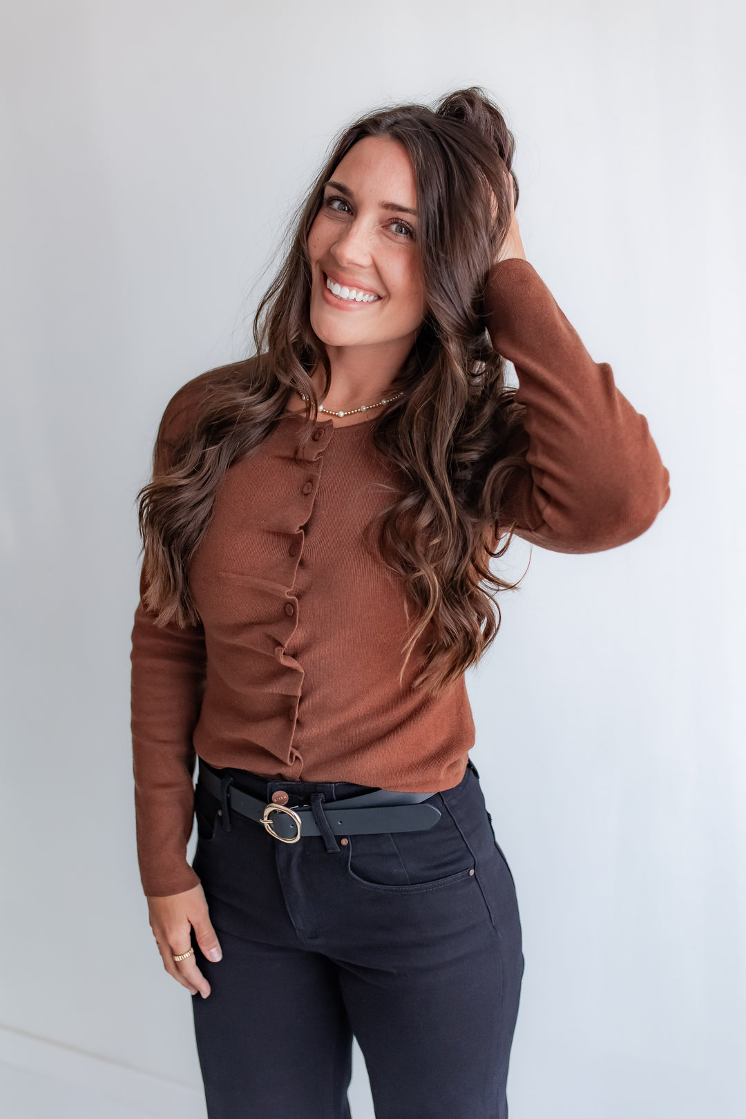 A woman wears a cocoa cinnamon-colored long-sleeve top with ruffles and fabric-covered buttons on the front.