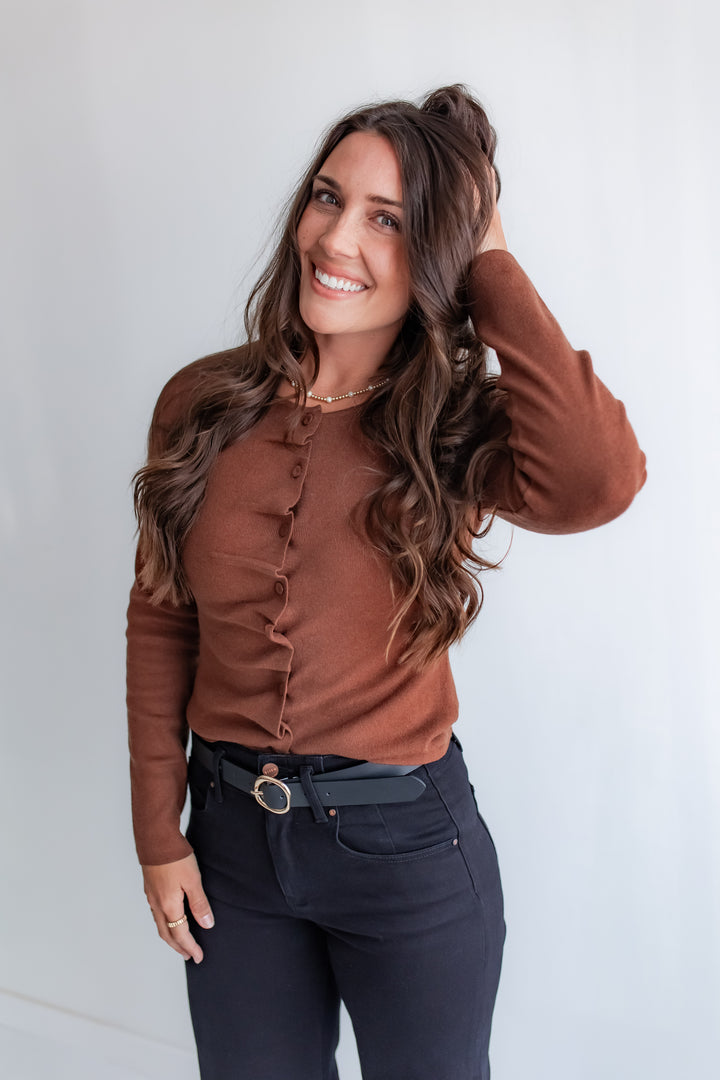 A woman wears a cocoa cinnamon-colored long-sleeve top with ruffles and fabric-covered buttons on the front.