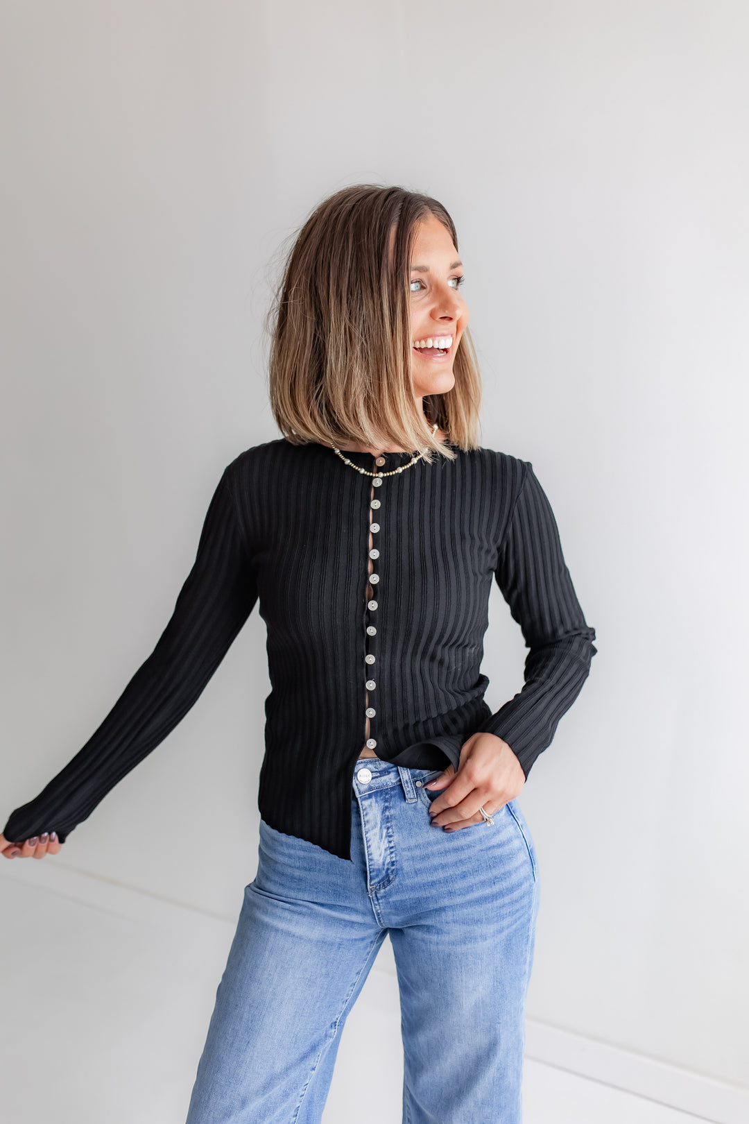 A woman wears a black long-sleeve crewneck top with full-length button details and a ribbed texture.