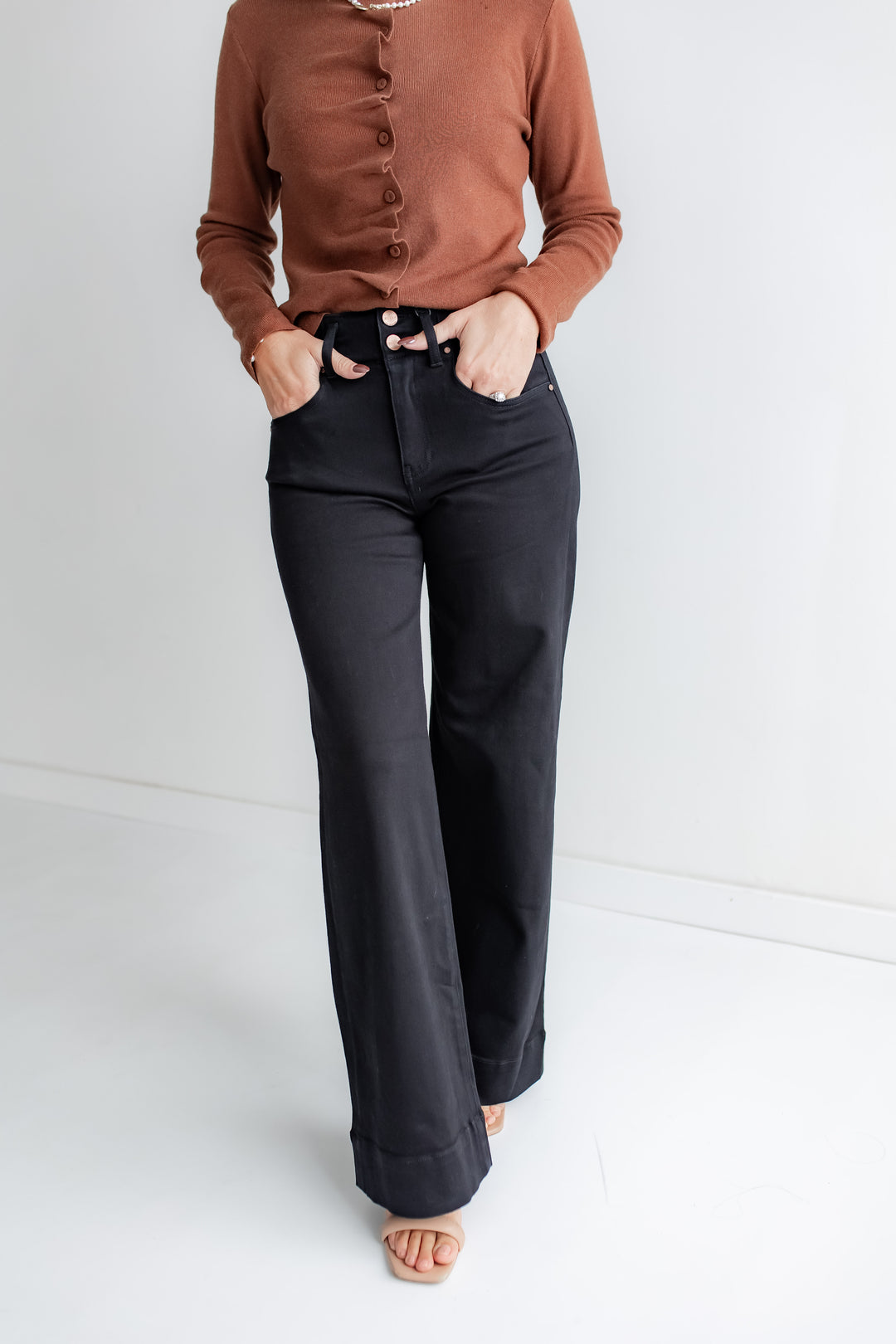 A woman wears a pair of black wide-leg denim jeans with a high-rise waist and a two-button closure.