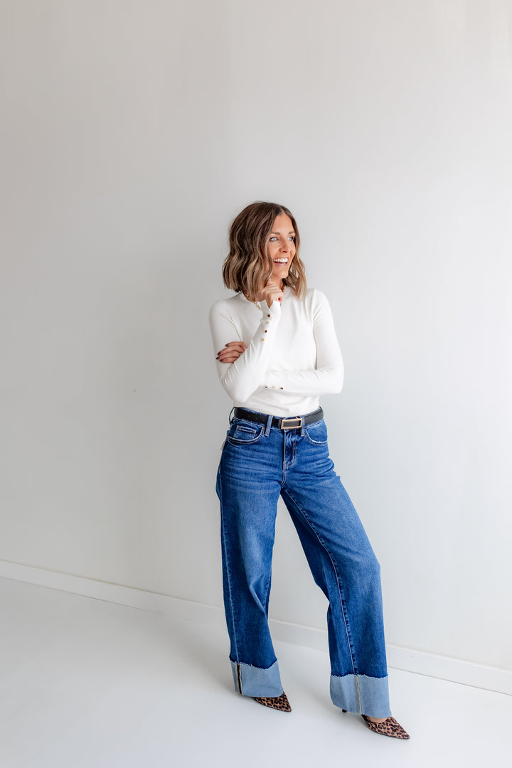 Woman wearing ivory blouse with gold button detail and cuff jeans. 