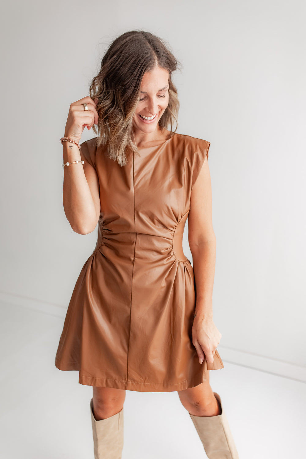 Close up of woman wearing a camel faux leather dress with ruching detail. 