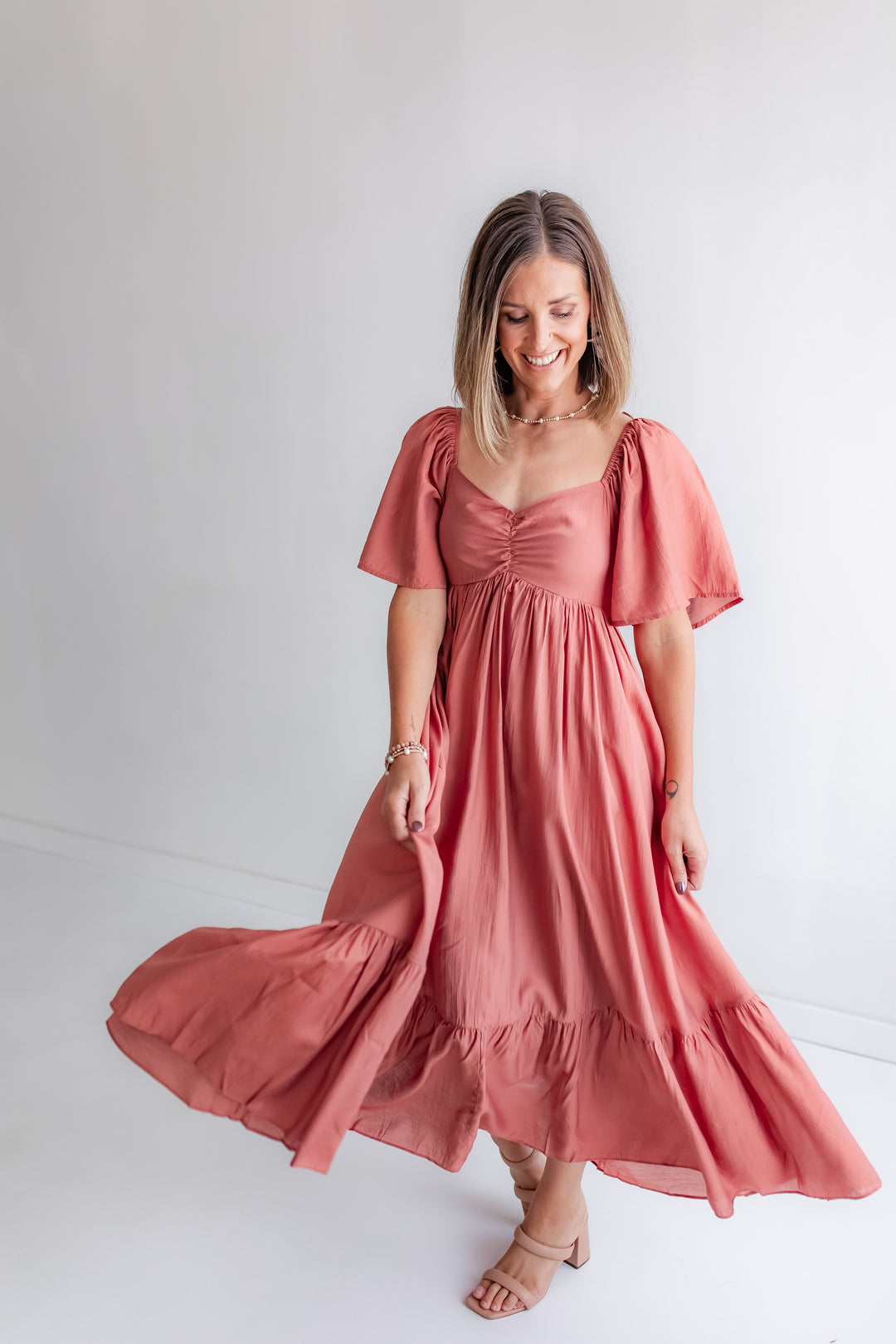 A woman wears a cinnamon-colored dress with a smocked back, a sweetheart bodice, and flutter sleeves.