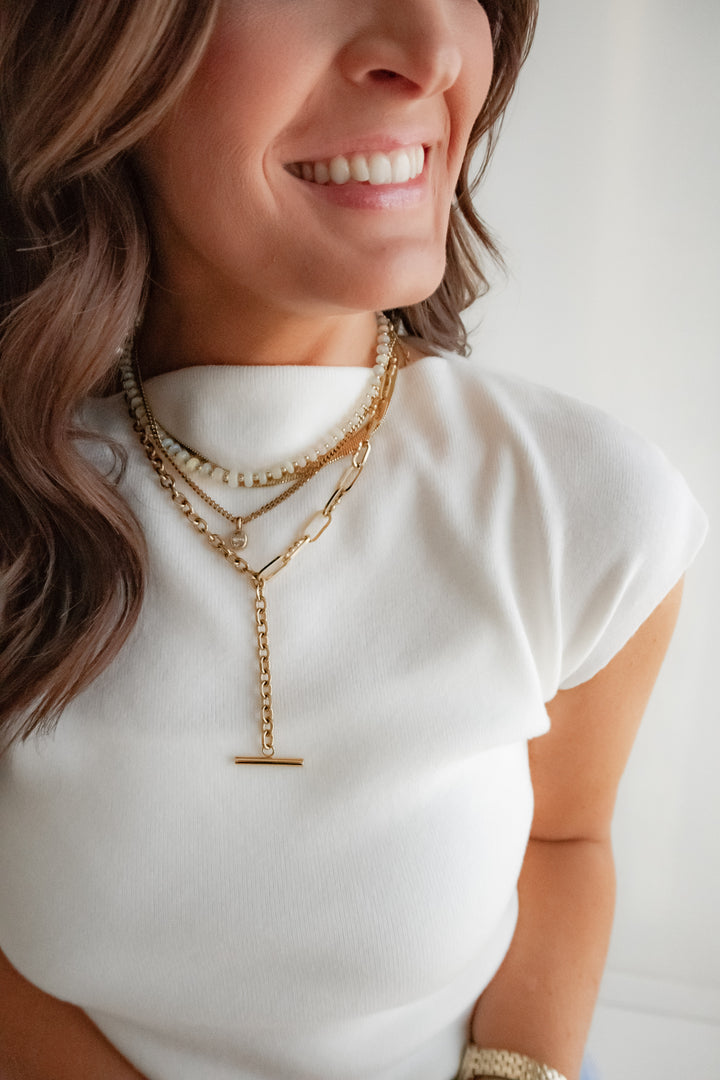 Woman wearing a white top and gold necklaces with a blurred background