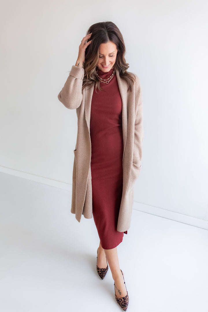 Woman wearing a burgundy dress with a beige cardigan against a white background