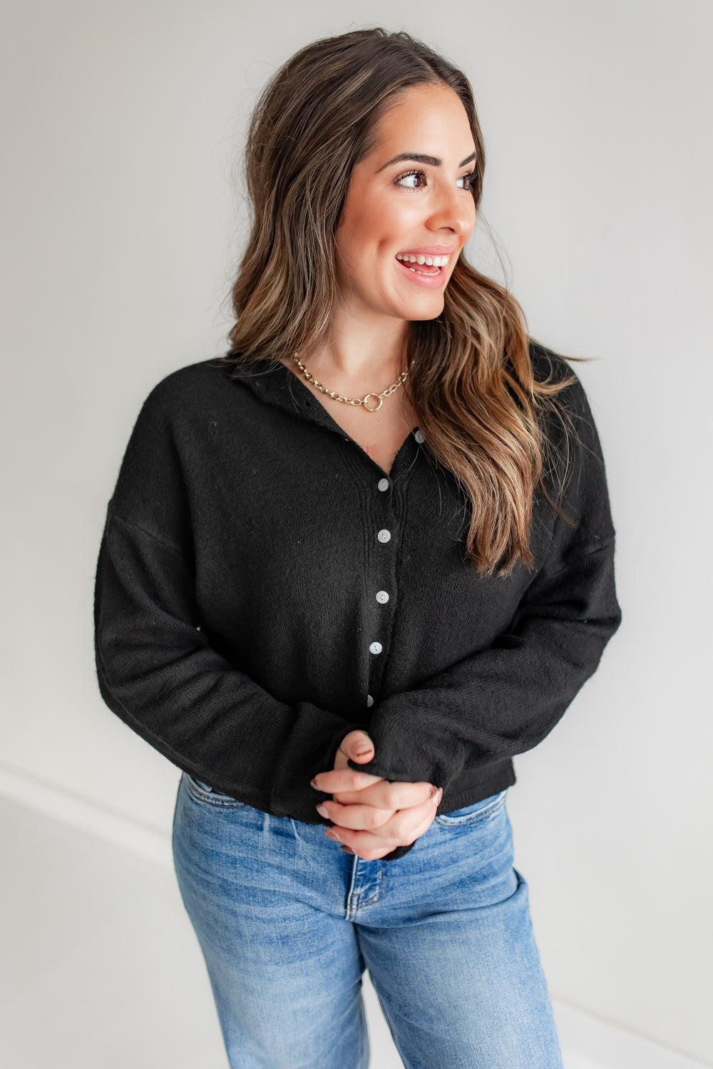 Woman wearing a black button-up cardigan and blue jeans.