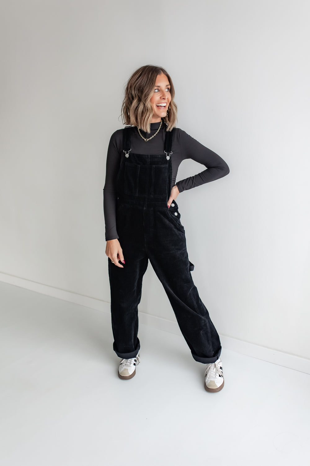 Woman wearing black corduroy overalls and a black long sleeve shirt.