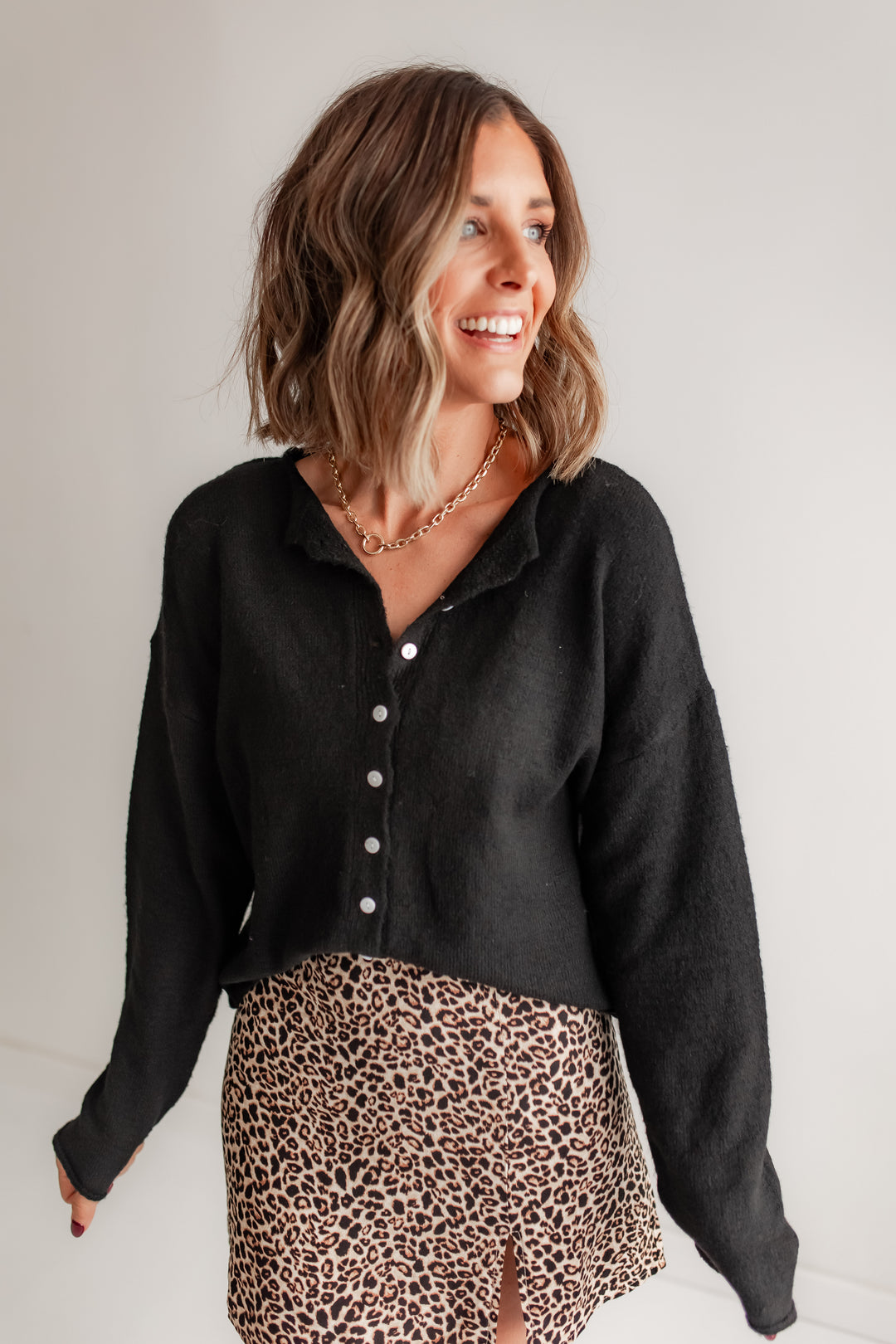 Woman wearing a black long sleeve cardigan with a leopard print skirt.