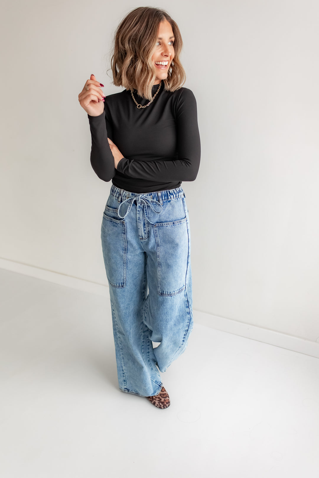 Woman wearing a black top and wide leg tie blue jeans against a white background