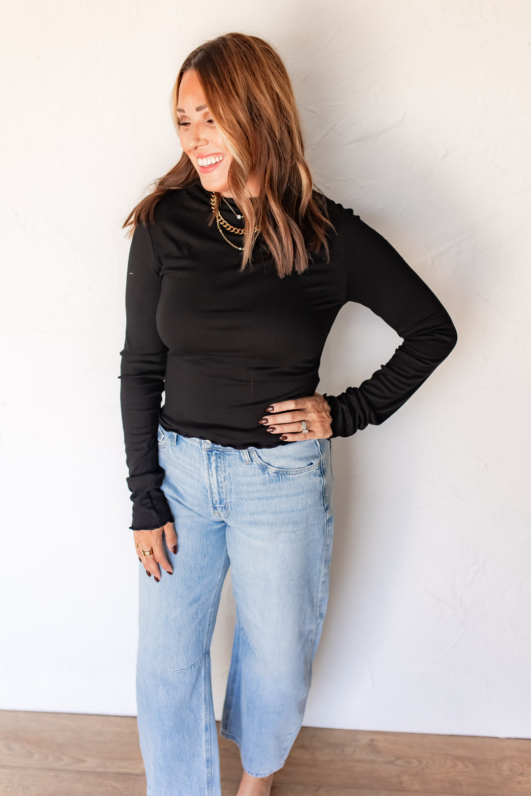 Woman wearing black fitted mockneck top with light wash denim and gold jewelry