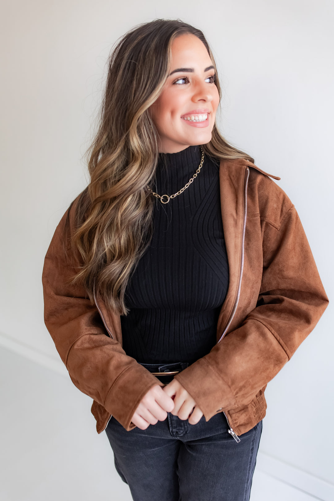 Woman wearing a brown suede jacket over a black turtleneck against a white background