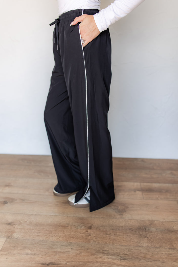 Close-up of black wide leg track pants with white contrast piping and side pocket