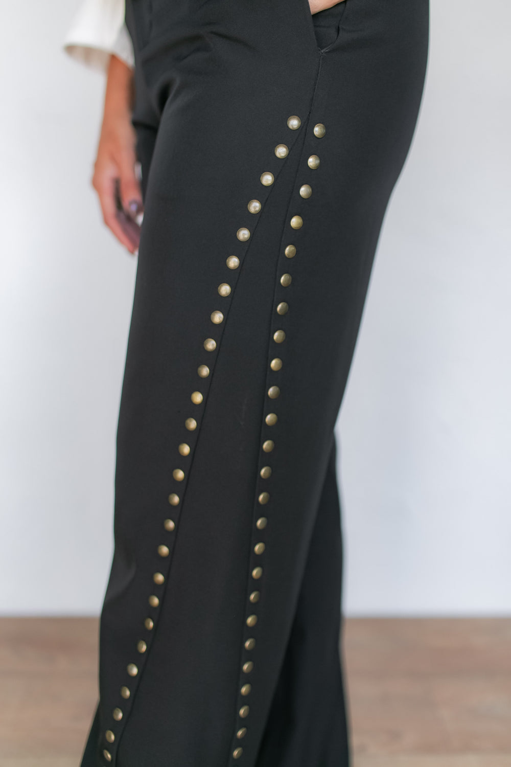 "Close-up of black wide leg pants with diagonal gold stud trim, styled with a lace blouse