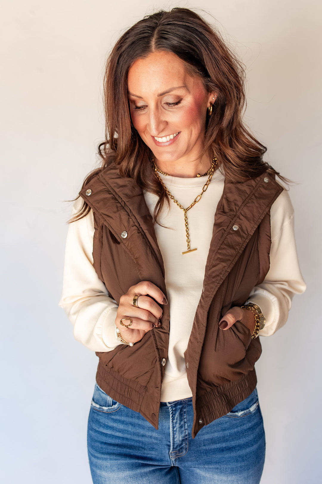 Woman wearing brown puffer vest with cream pullover and medium wash denim