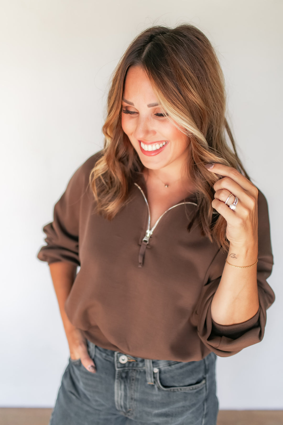 Woman wearing brown cropped quarter zip pullover with balloon sleeves and washed denim