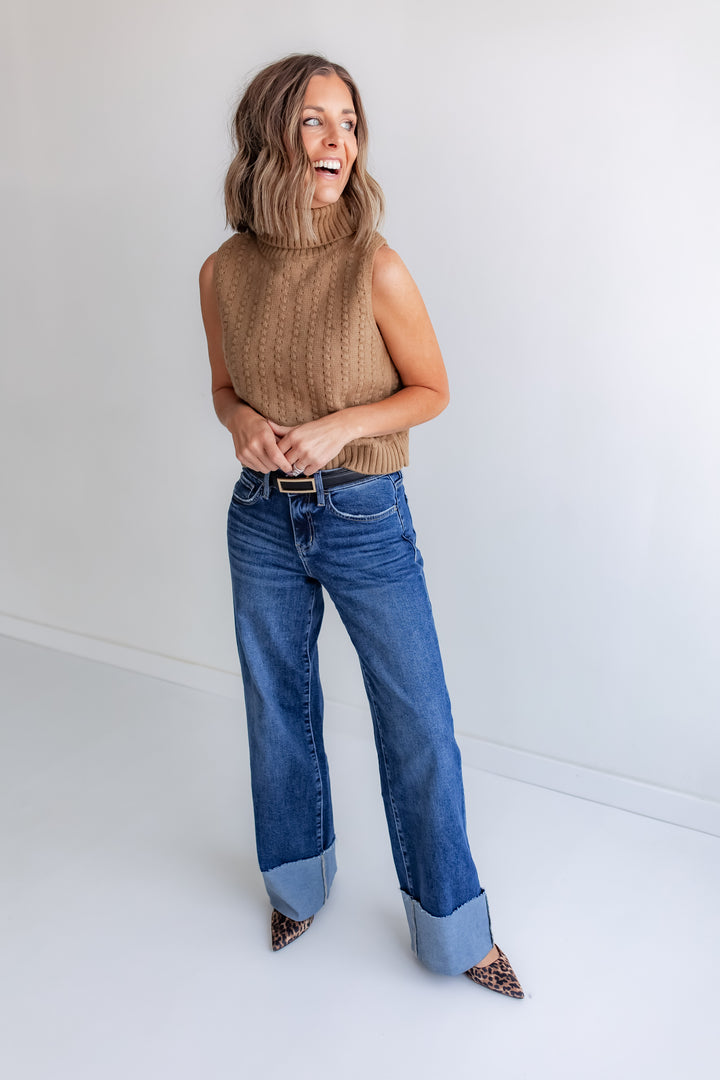 Woman wearing a Brown sleeveless knit top with turtleneck and dark denim jeans. 