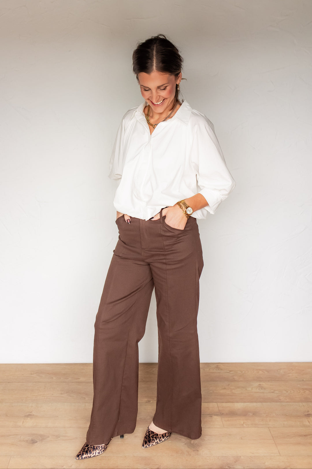 Full front view of brown wide leg high-waisted trousers styled with white button down blouse