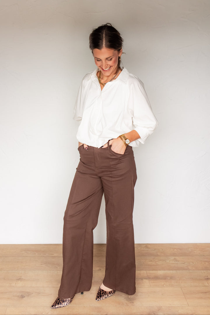 Full front view of brown wide leg high-waisted trousers styled with white button down blouse