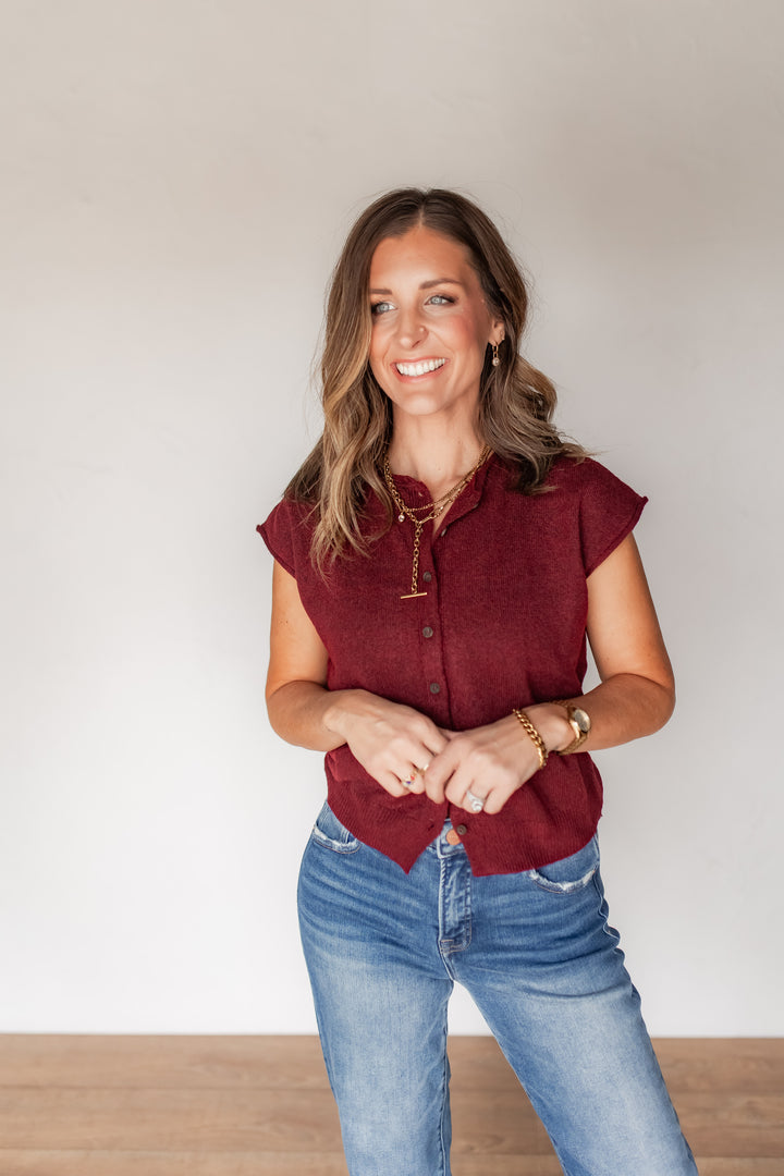 Woman wearing burgundy knit cap sleeve cardigan top buttoned up with medium washed denim