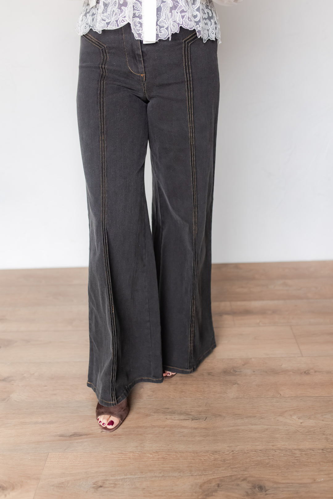 Woman wearing charcoal wide leg denim pants with contrast stitching, styled with a lace blouse