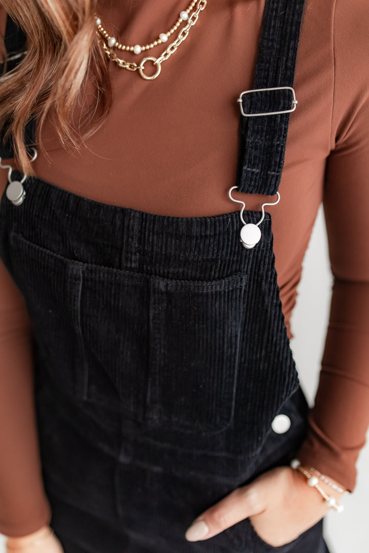 Close up of black corduroy overalls with brown top. 
