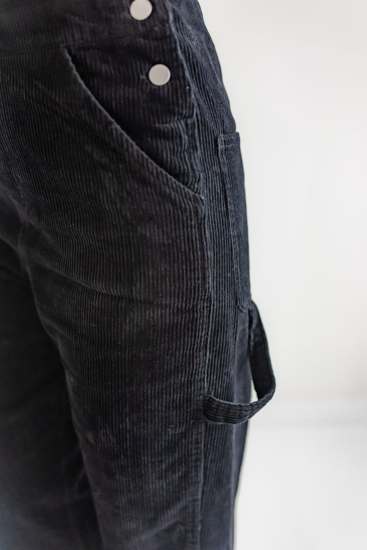 Black corduroy pants with button details on a white background