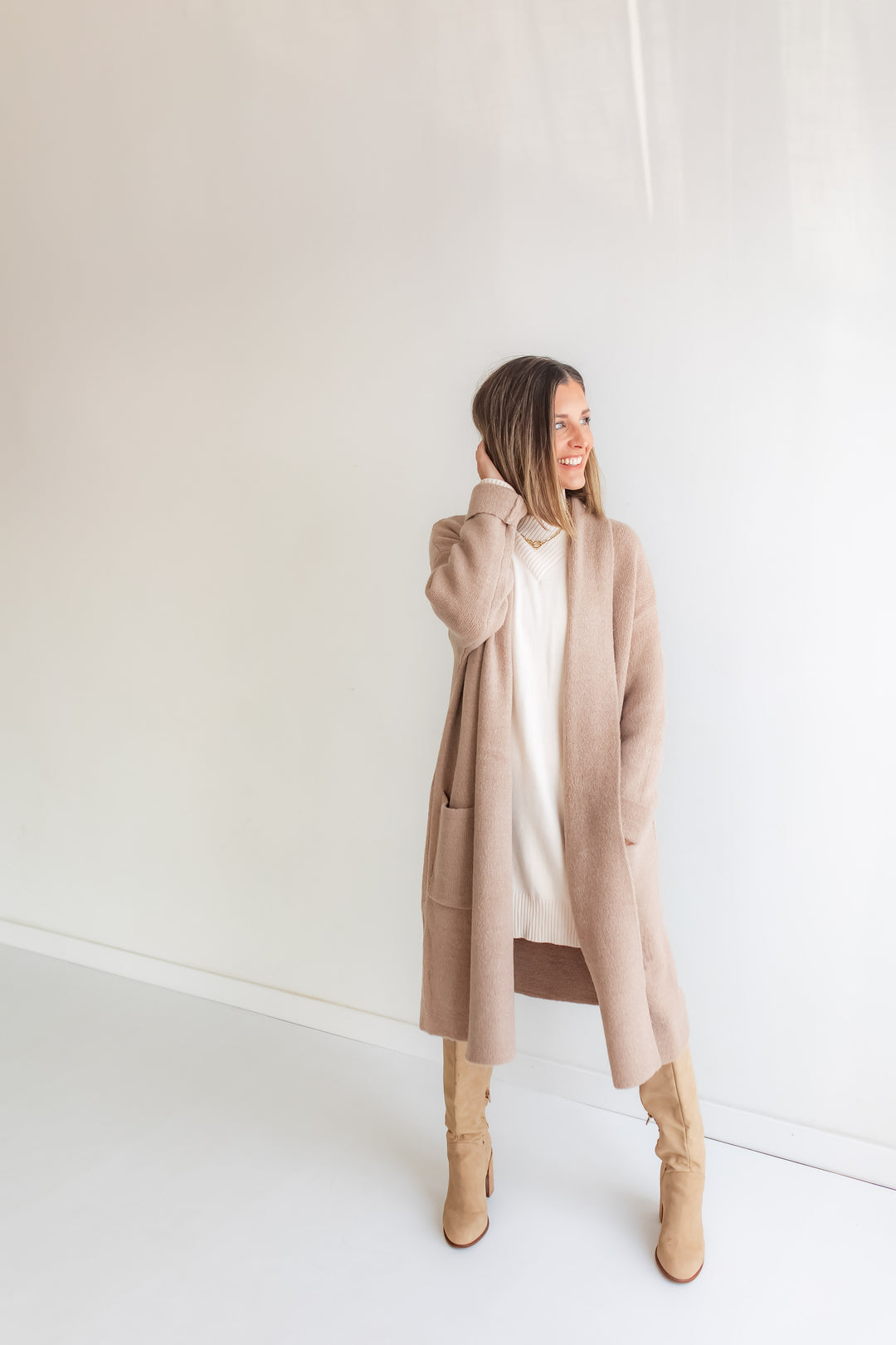 Woman wearing a long taupe cardigan over a cream sweater dress.