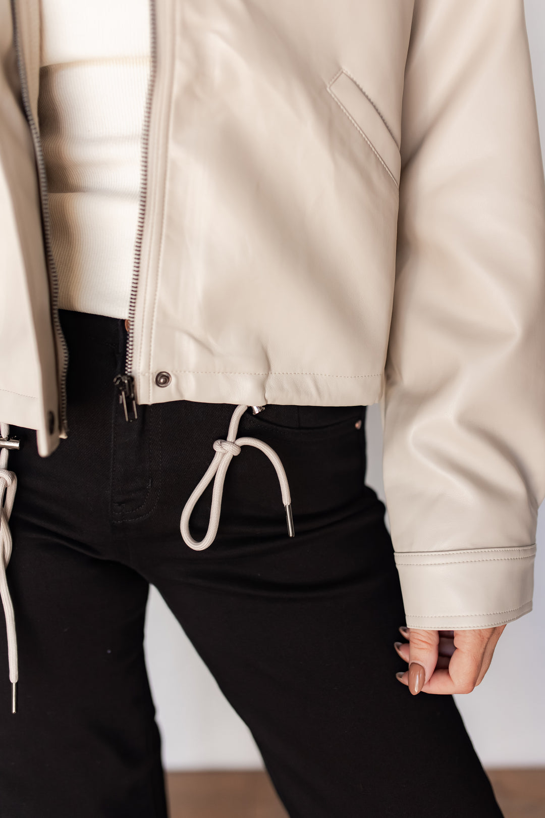 : "Close-up of cream faux leather jacket drawstring and zipper detail
