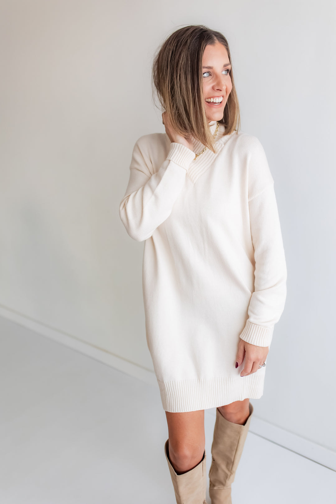 Woman wearing a cream sweater dress with tan tall boots. 