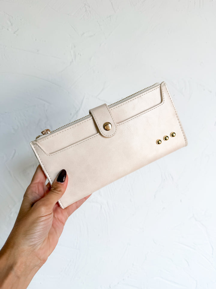Cream vegan leather wallet with gold snap-tab closure and stud detail, held in hand