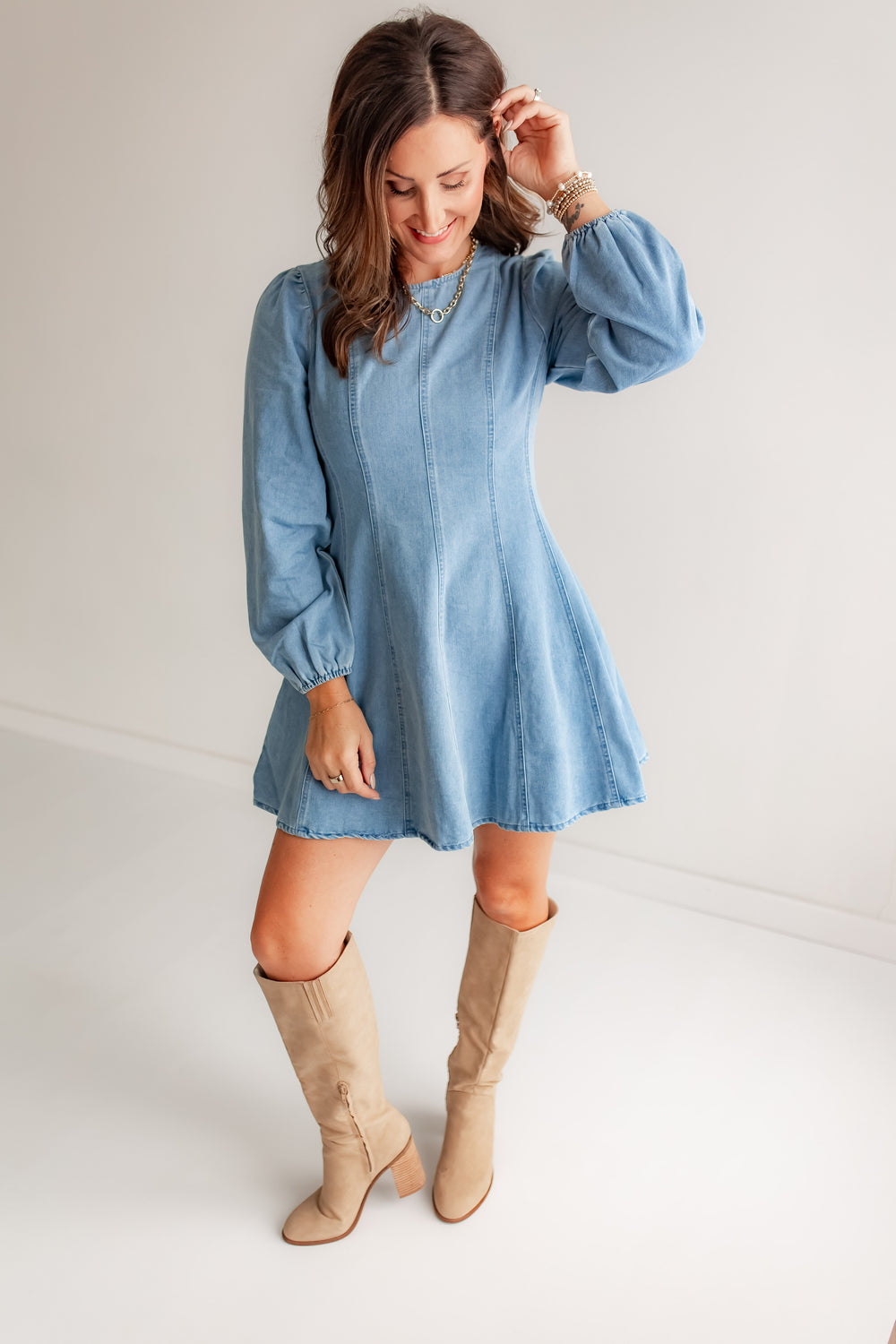 Woman wearing a light blue denim dress with long sleeves and beige knee-high boots