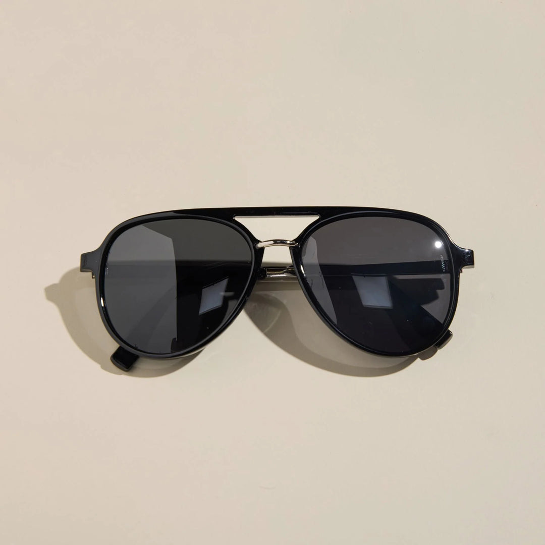 Black aviator sunglasses with silver nose accent on a beige background