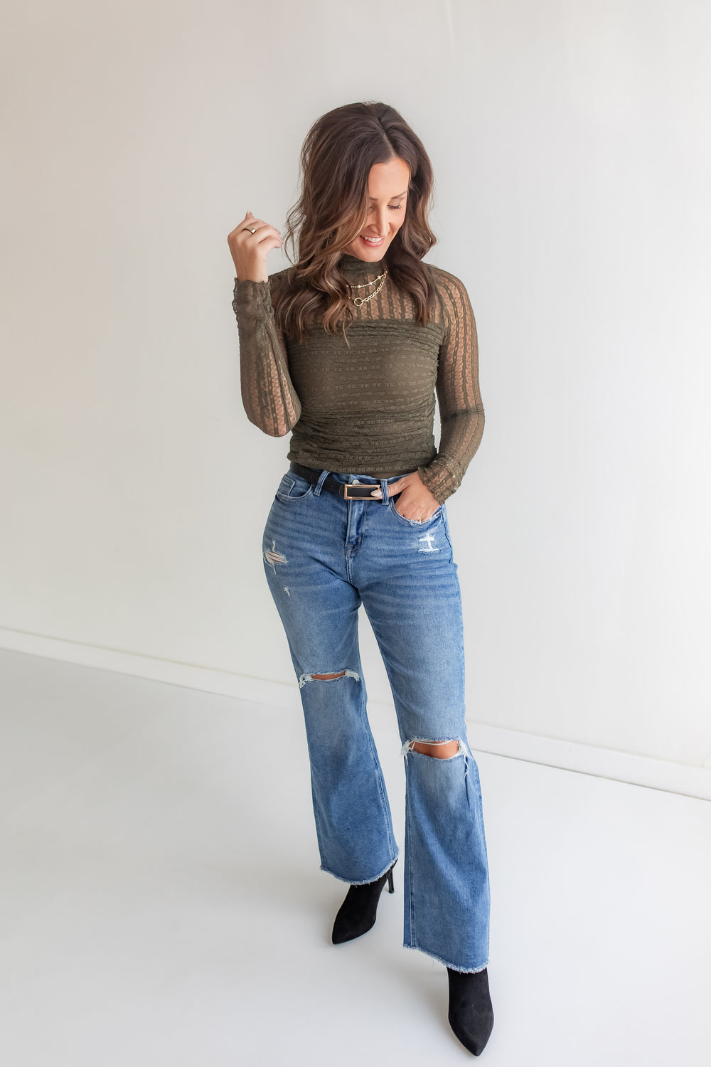 Woman wearing an olive lace bodysuit and blue jeans against a white background