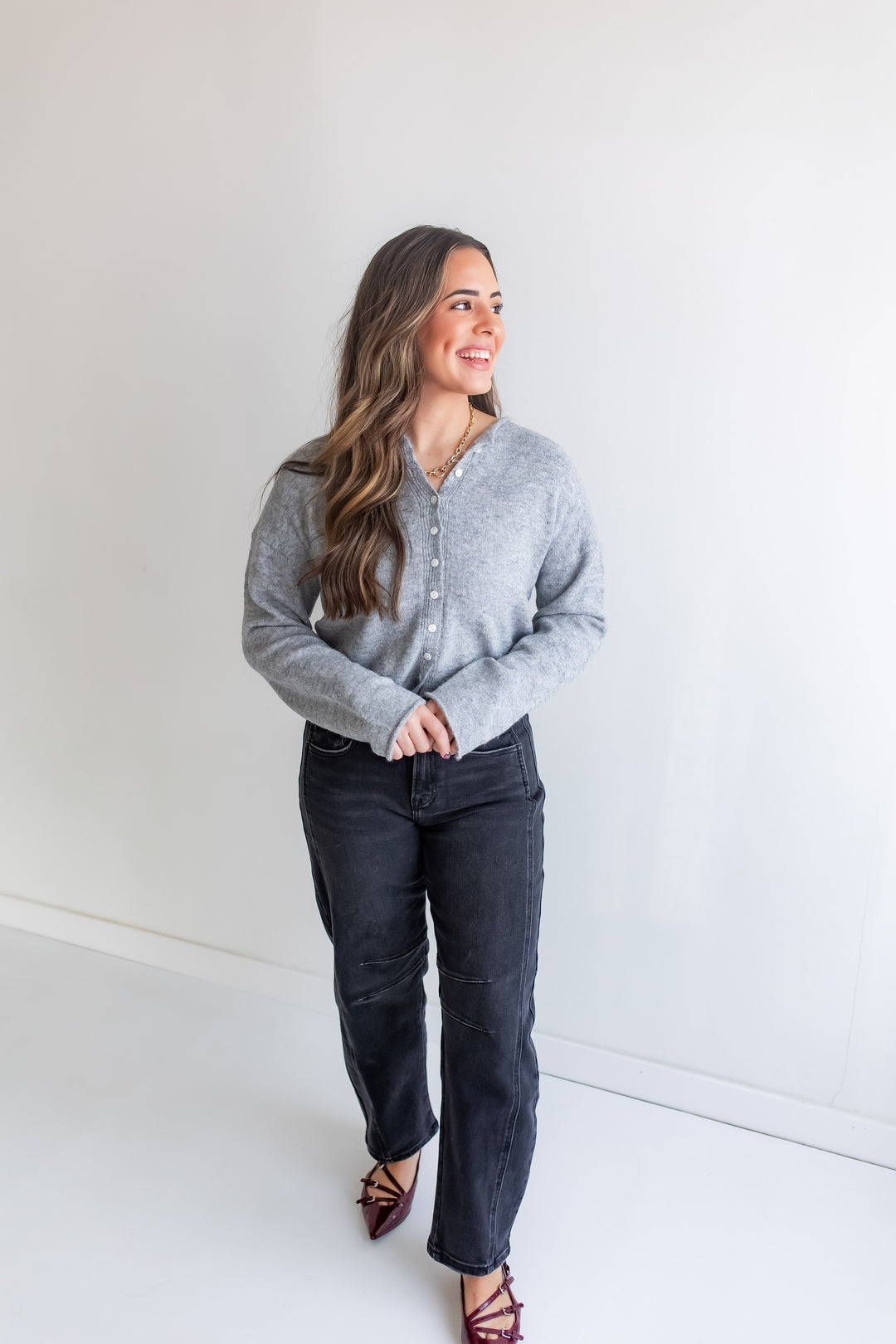 Woman wearing a gray button up cardigan sweater and dark jeans.