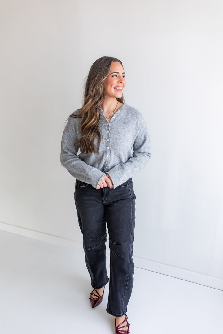 Woman wearing a gray button up cardigan sweater and dark jeans.