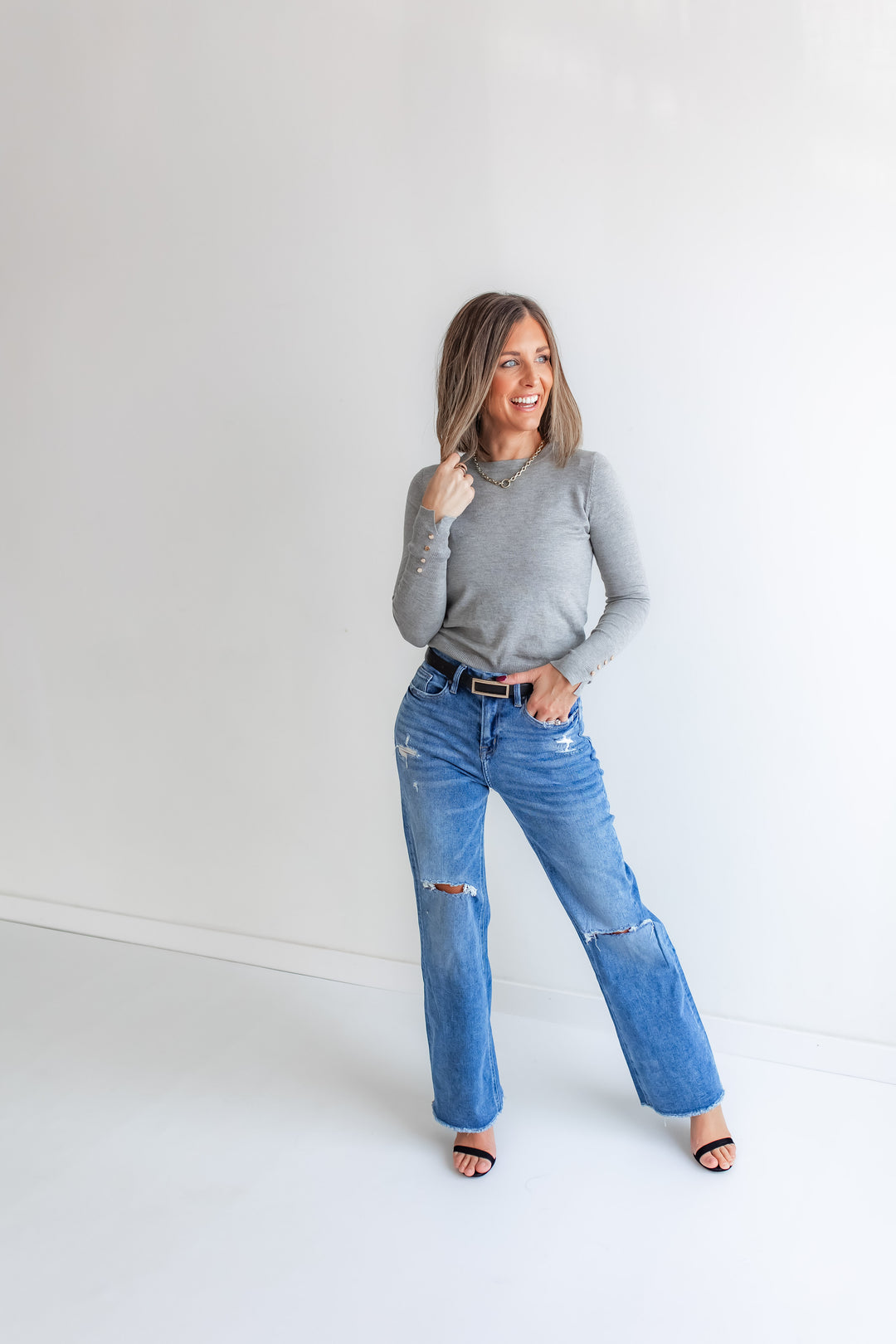 Woman wearing a gray sweater and blue jeans against a white background