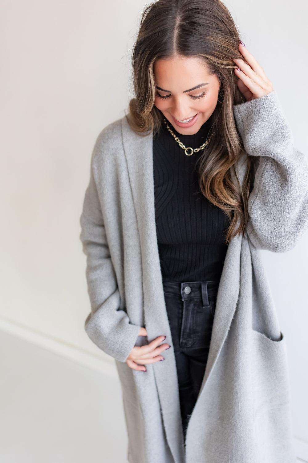 Woman wearing a gray cardigan over a black outfit with a plain background