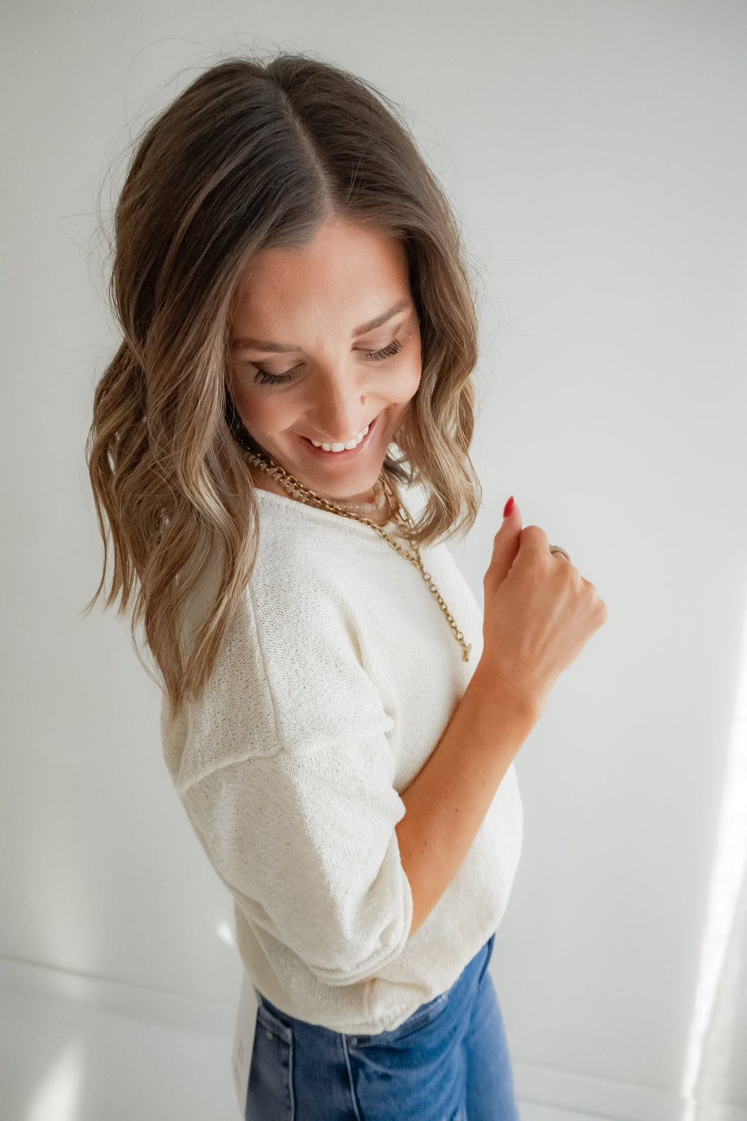 Woman wearing a white sweater and blue jeans against a plain background