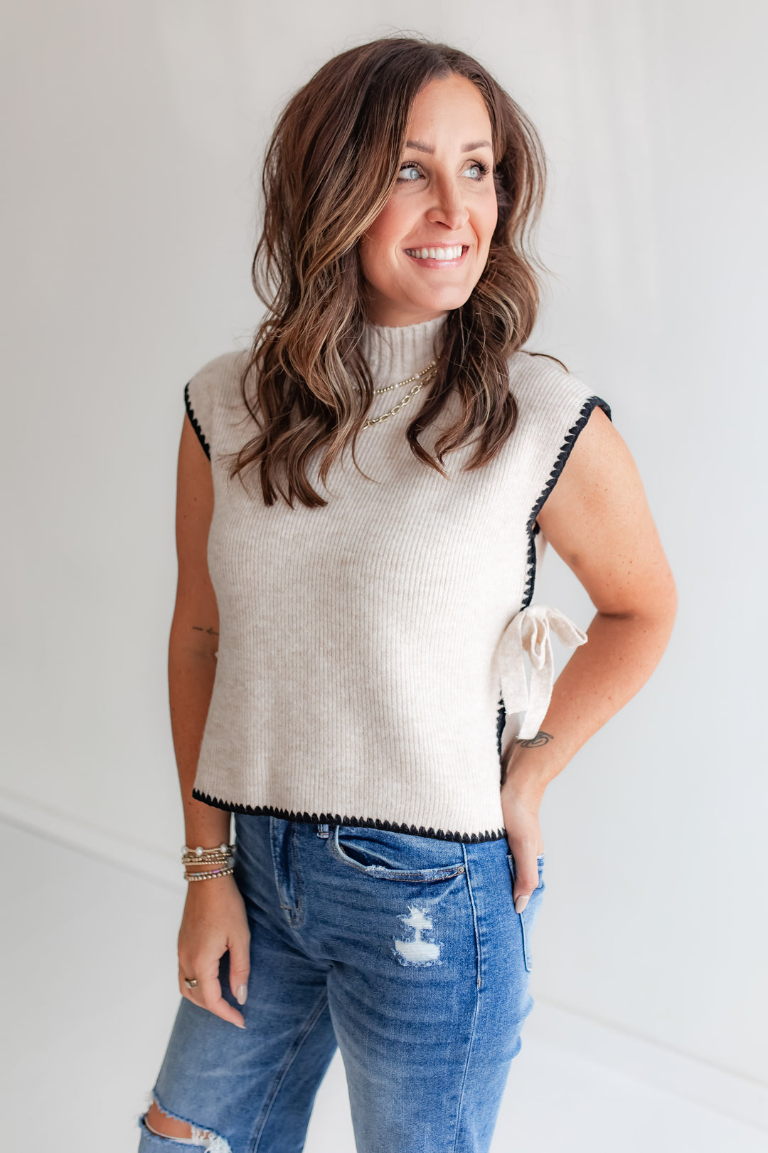 Ivory sleeveless sweater with black contrast stitching with medium wash mica denim 