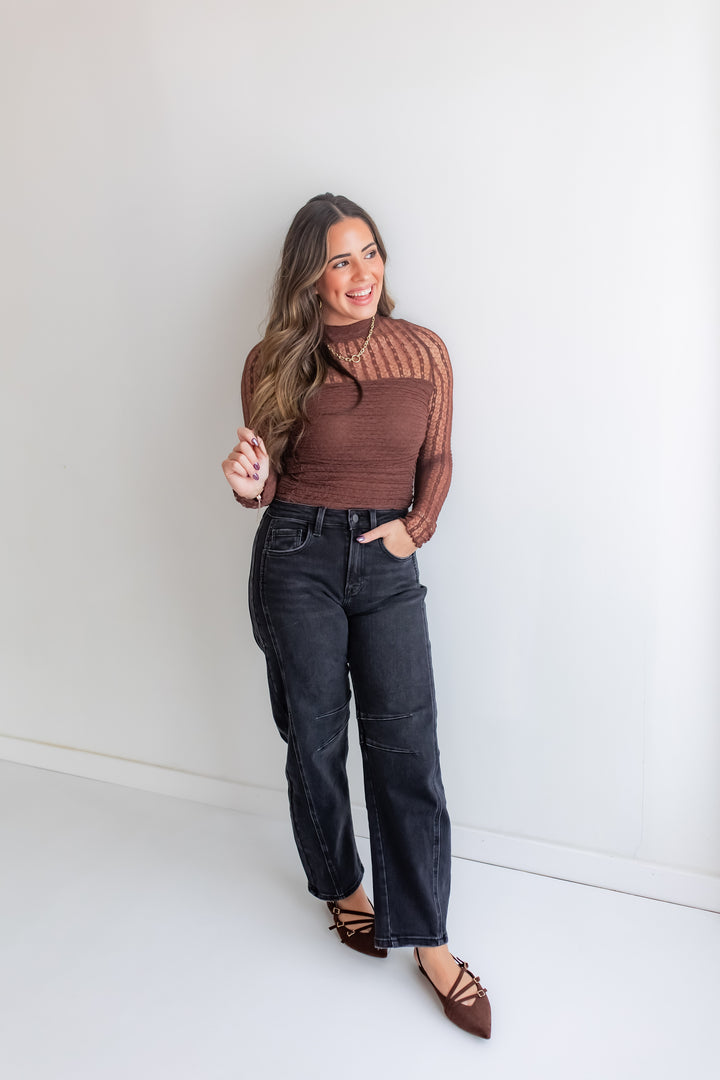 Woman wearing a brown lace bodysuit and black jeans against a white background