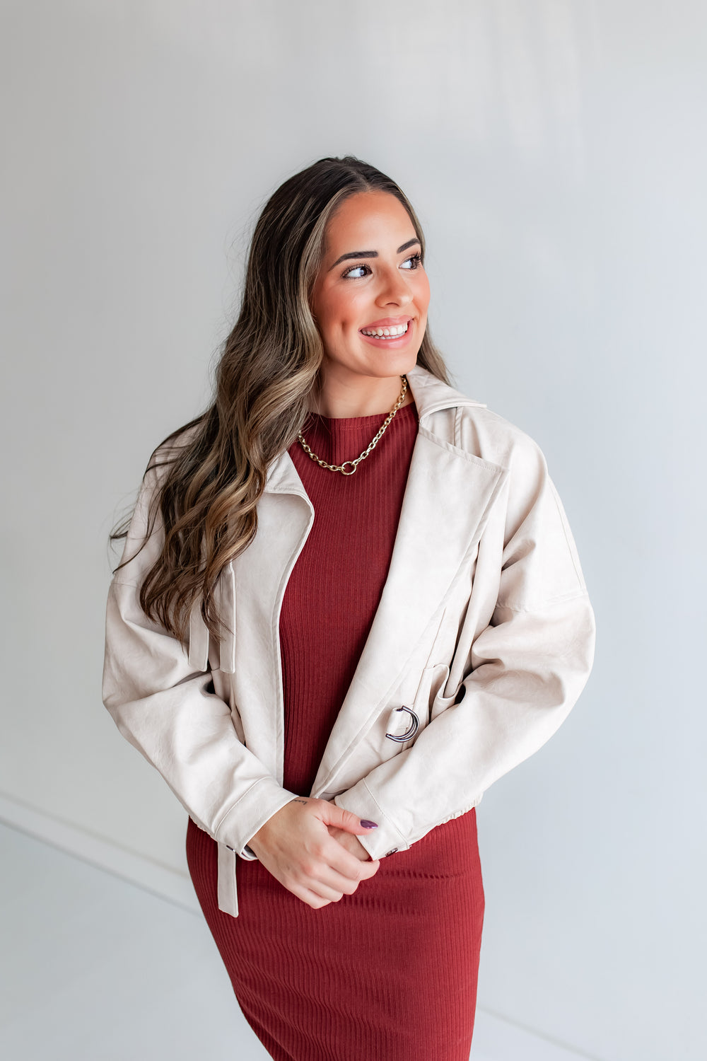 Woman wearing an ivory leather jacket over a red dress against a white background
