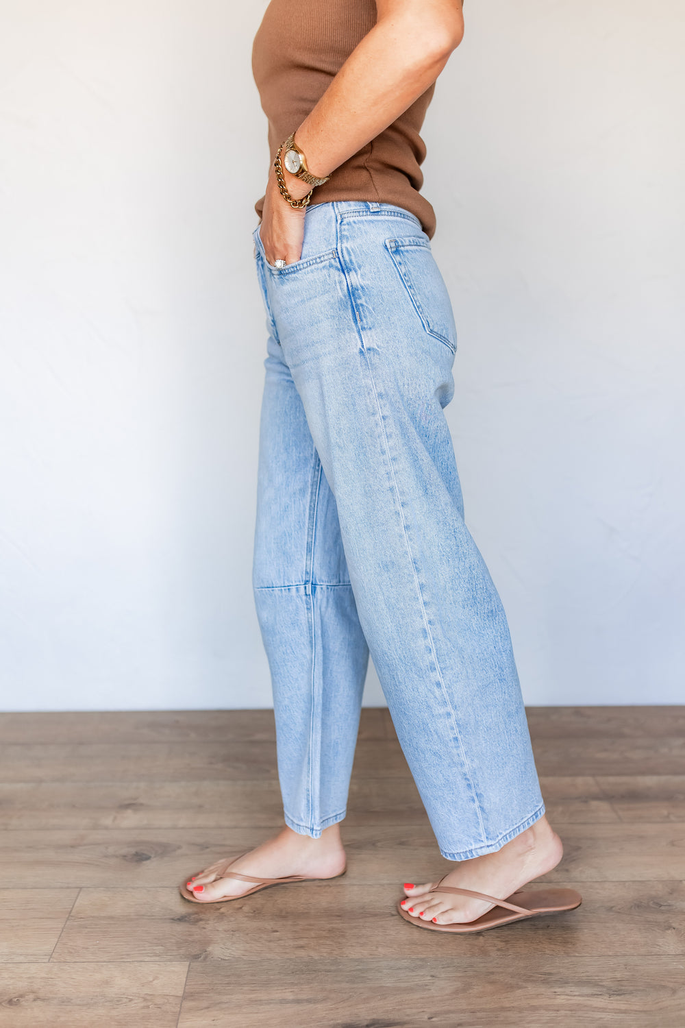 Side profile of light wash barrel leg jeans showing curved seam silhouette