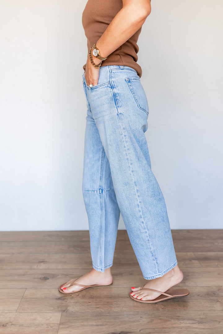 Side profile of light wash barrel leg jeans showing curved seam silhouette