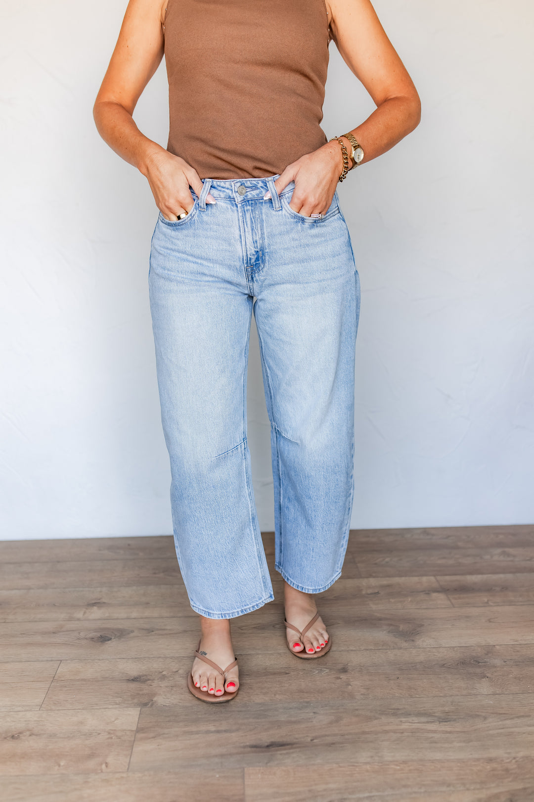 Woman styling light wash barrel leg jeans with brown ribbed tank and sandals