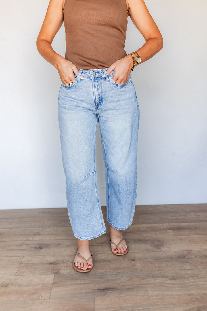 Woman styling light wash barrel leg jeans with brown ribbed tank and sandals