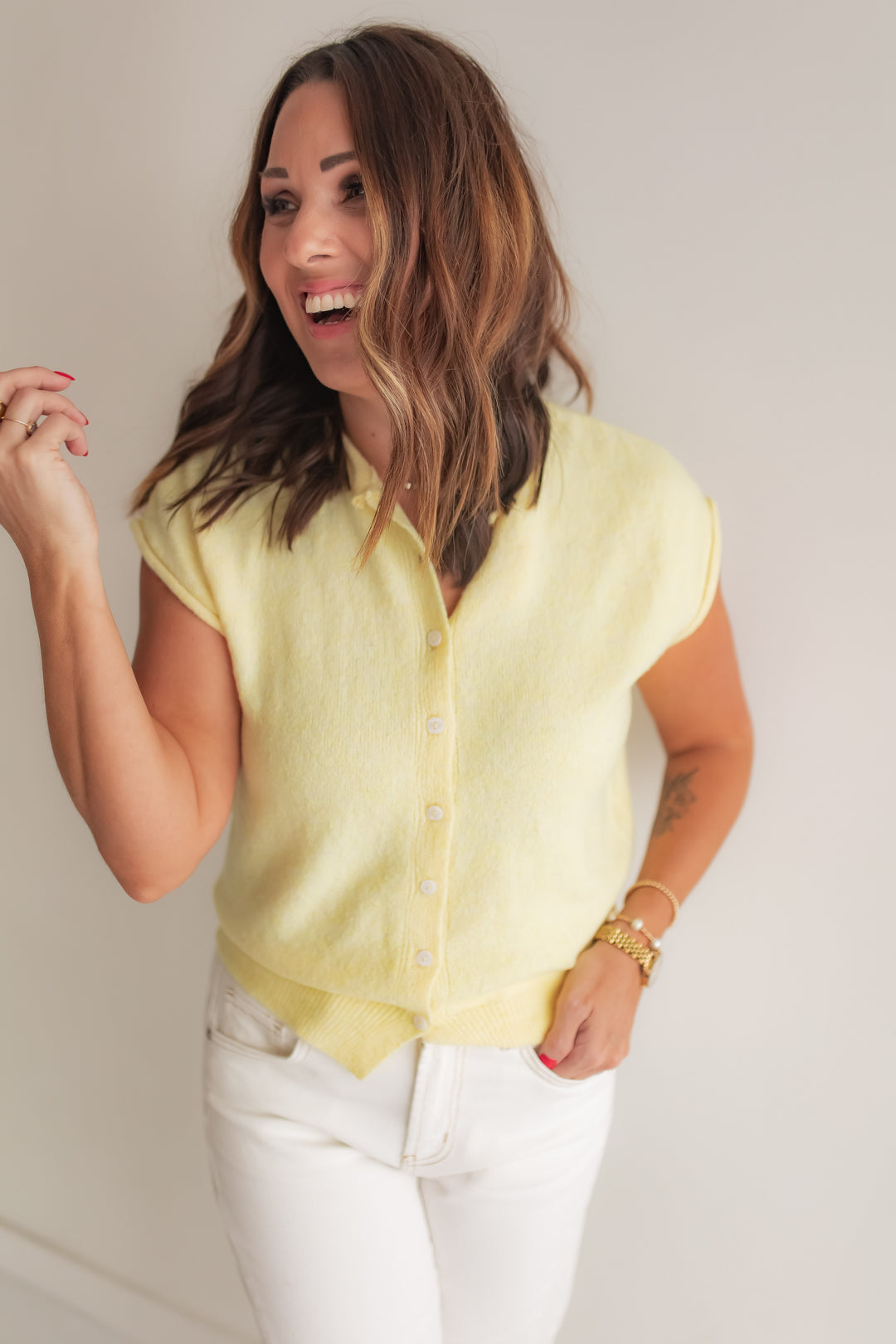 Woman wearing a light yellow button up cardigan styled with white pants for a spring outfit