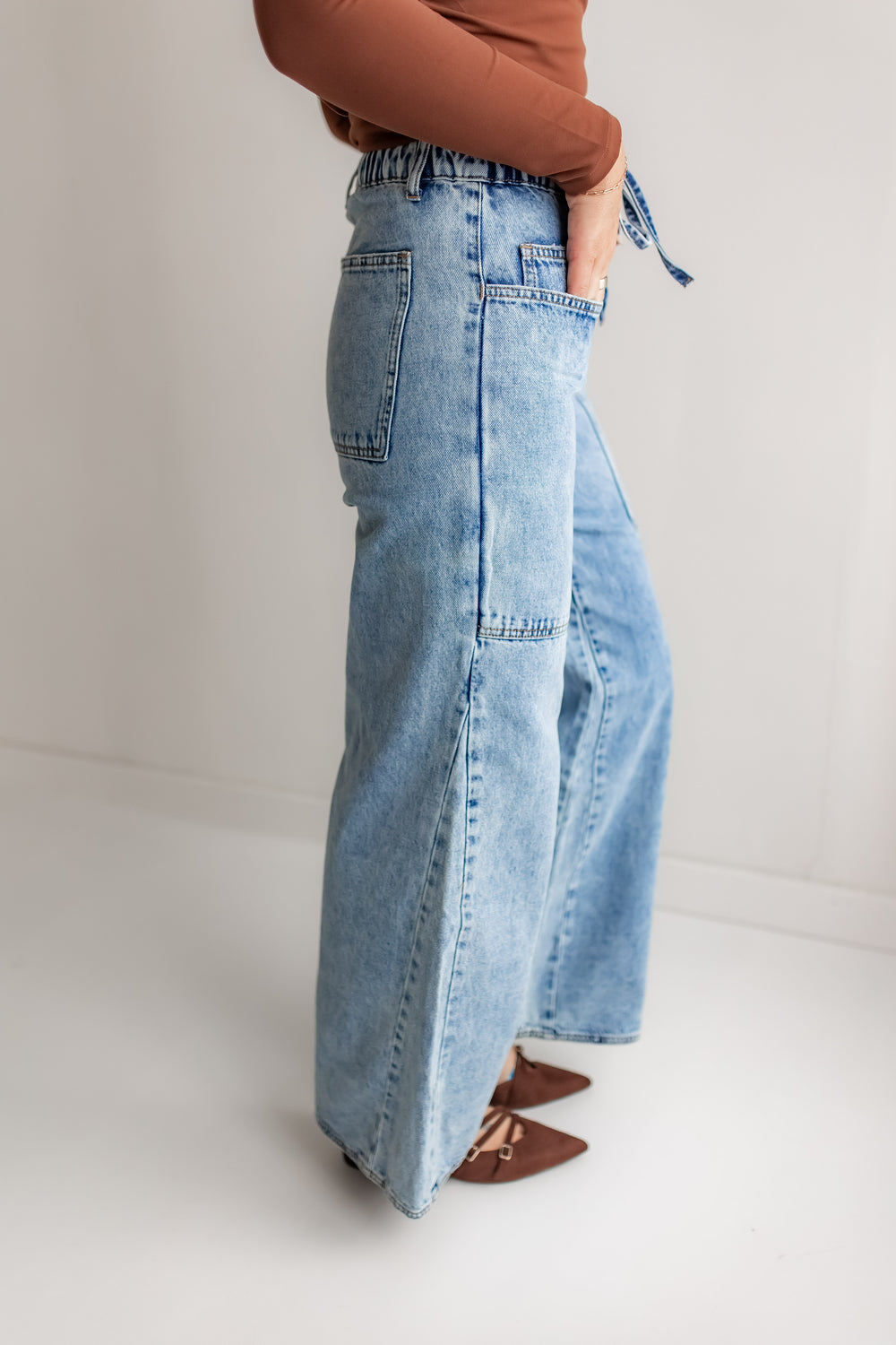 Woman wearing light blue wide-leg jeans and a brown top on a white background